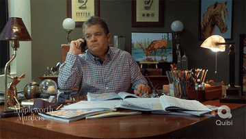Patton Oswalt, on the phone, suddenly looks at his lap behind a desk.