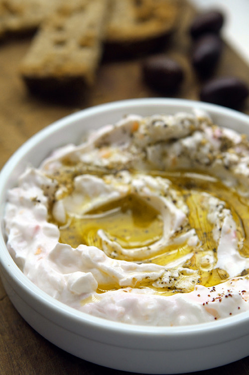 A bowl full of a creamy yogurt-based dip, topped with a healthy drizzle of rich olive oil and flecks of spices