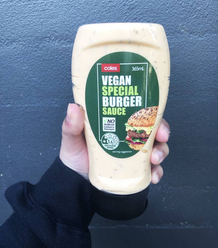 A hand holding the Vegan Special Burger Sauce from Coles against a brick wall