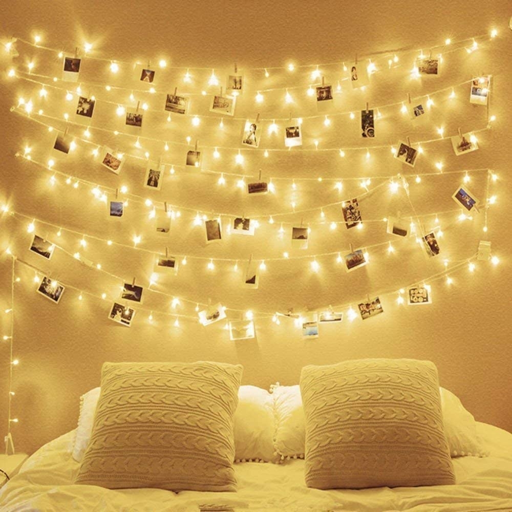 Fairy lights and photos hanging on a wall behind a bed