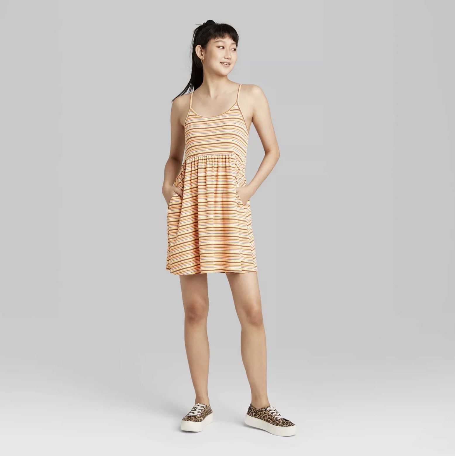 Model is wearing an orange babydoll dress with thin shoulder straps and stripes in different shades of orange