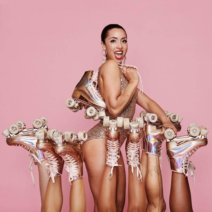 A model wears a glittery bodysuit and drapes a pair of metallic Impala roller skates over her shoulder. She is surrounded by five pairs of the same roller skates