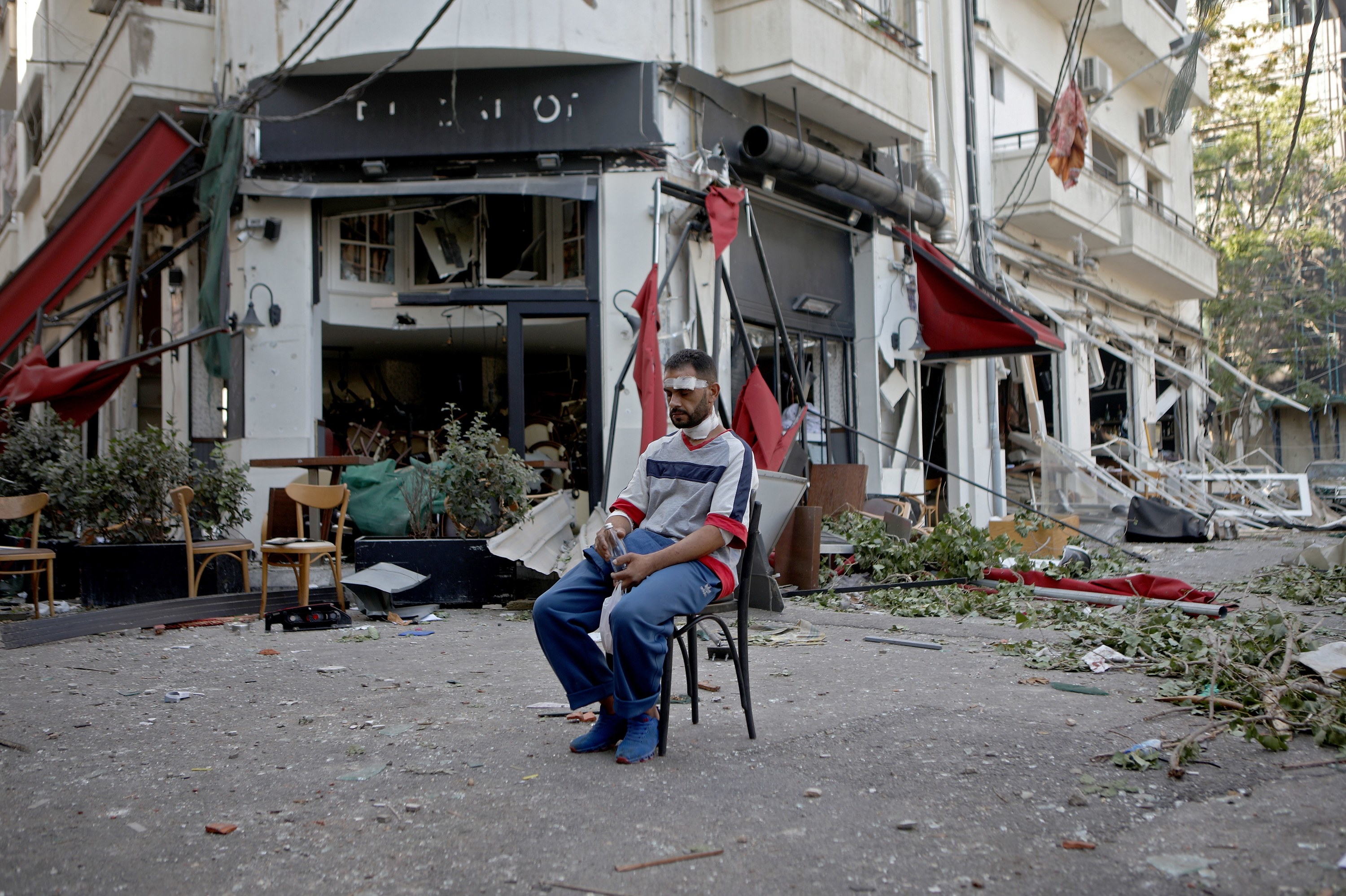 A man with a bandaged head sits alone in the middle of a destroyed street