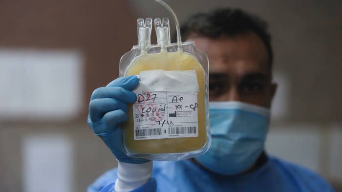 A male nurse wearing a surgical mask holds a bag of yellow plasma