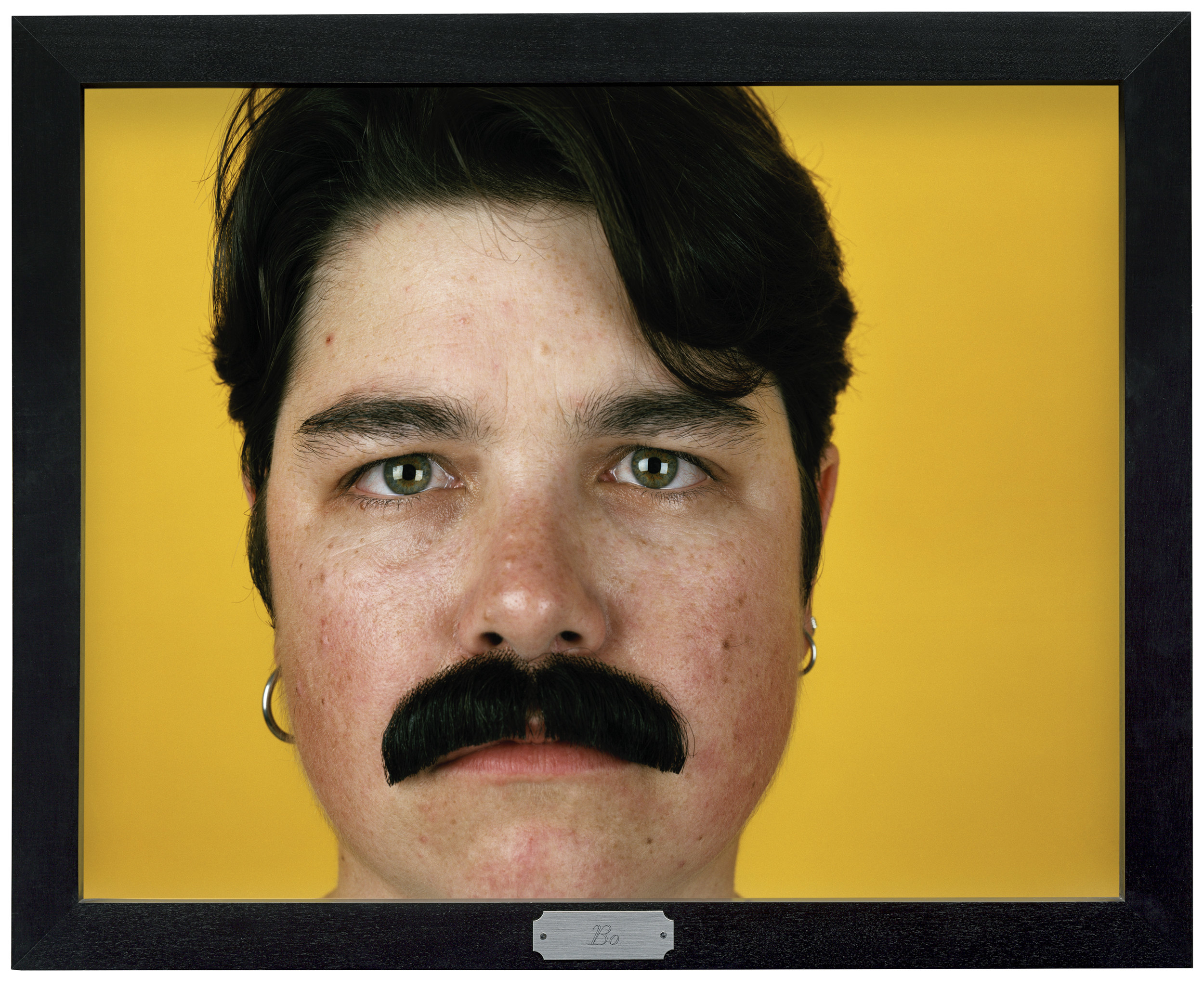 A man with a moustache and earrings on a yellow background