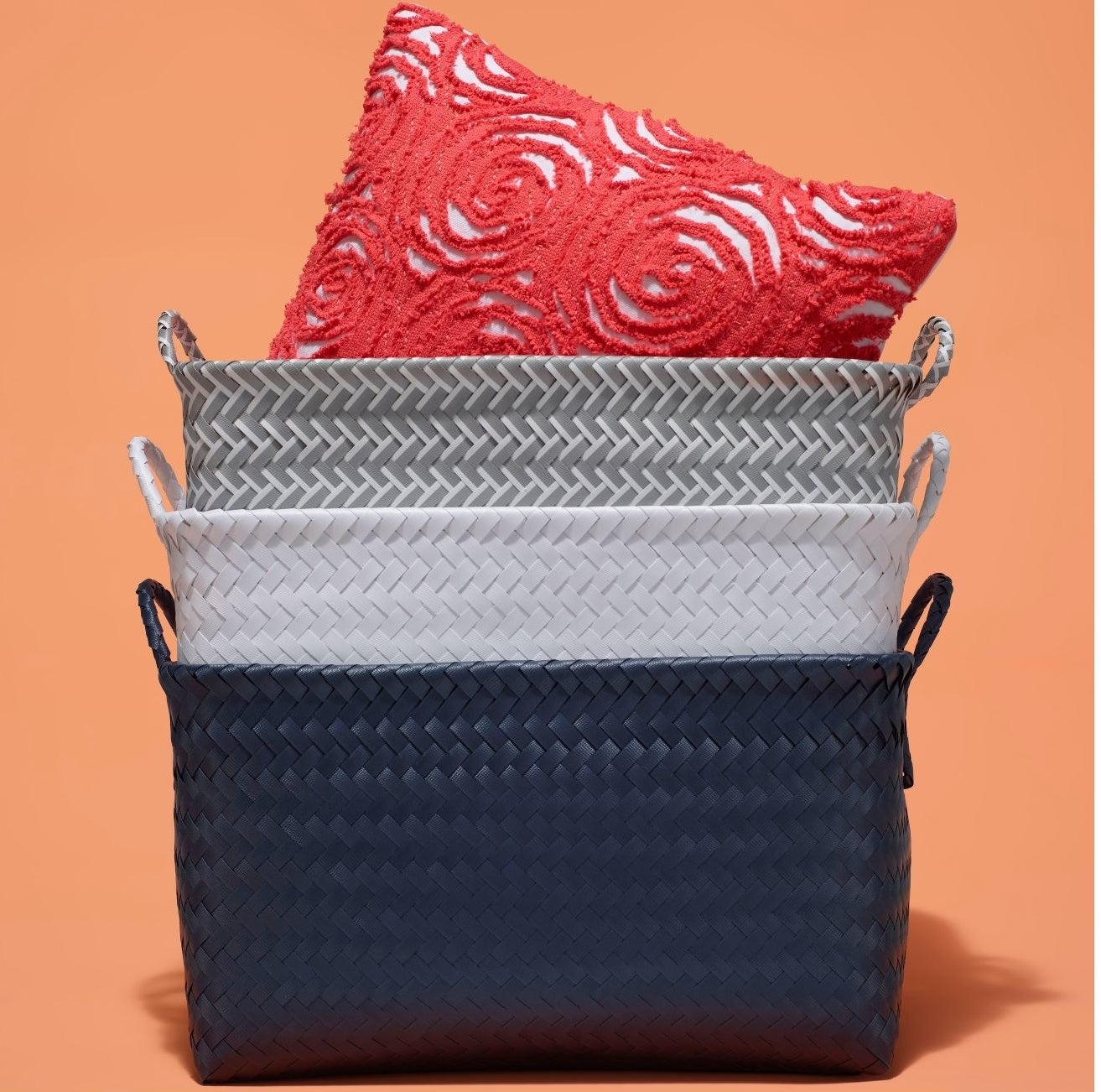 The woven rectangular baskets in navy, white, and gray in a stack with a throw pillow in the top one
