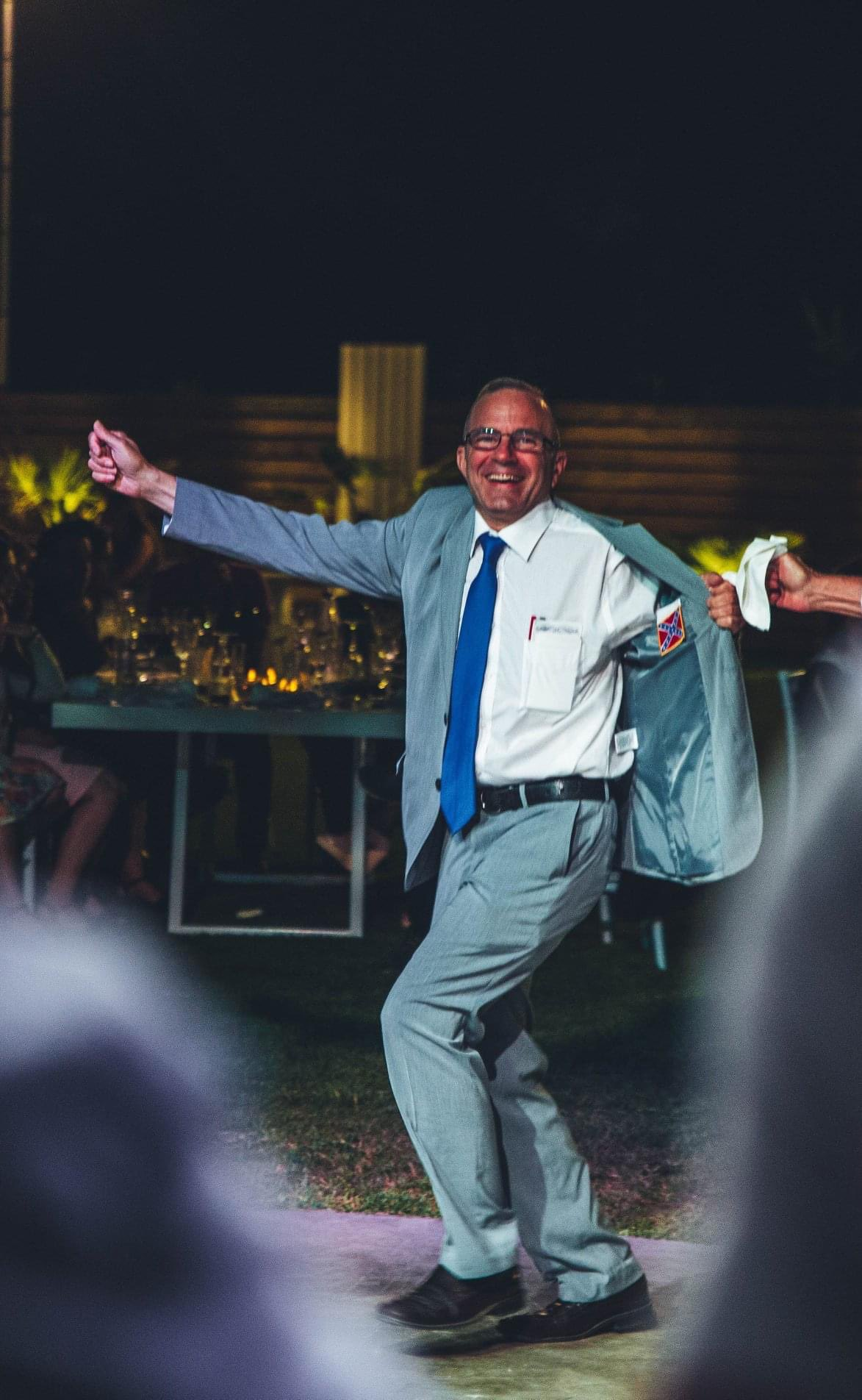 Koletas dancing while holding open his suit jacket to reveal a confederate flag