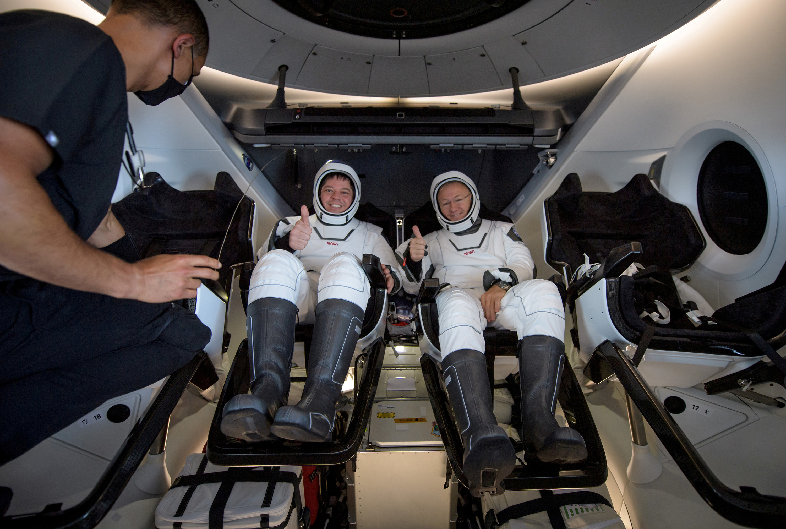 Two astronauts smile and give a thumbs-up as a man enters the capsule