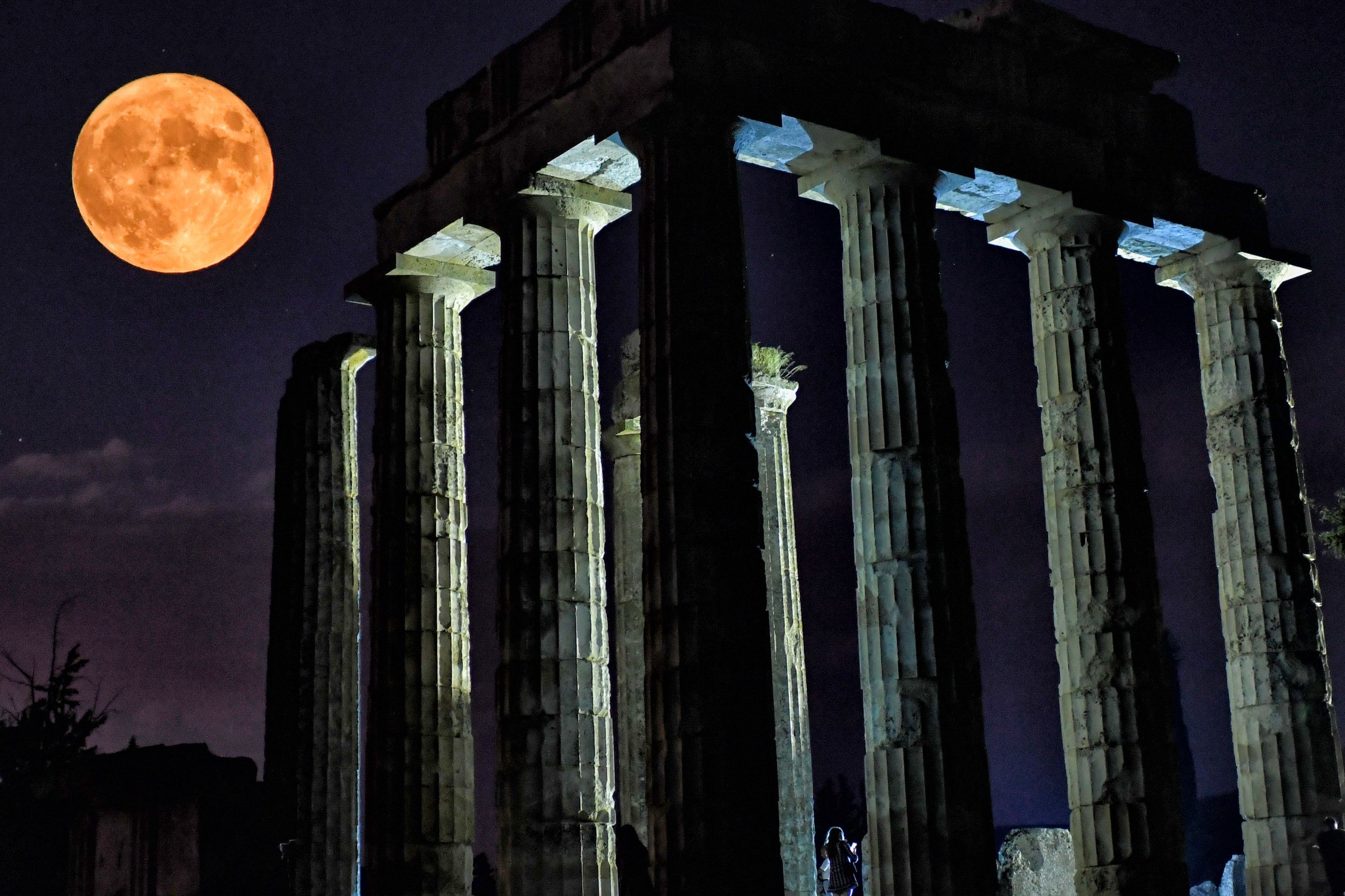 A full orange moon rises over the ruins of a colossal temple with gigantic columns