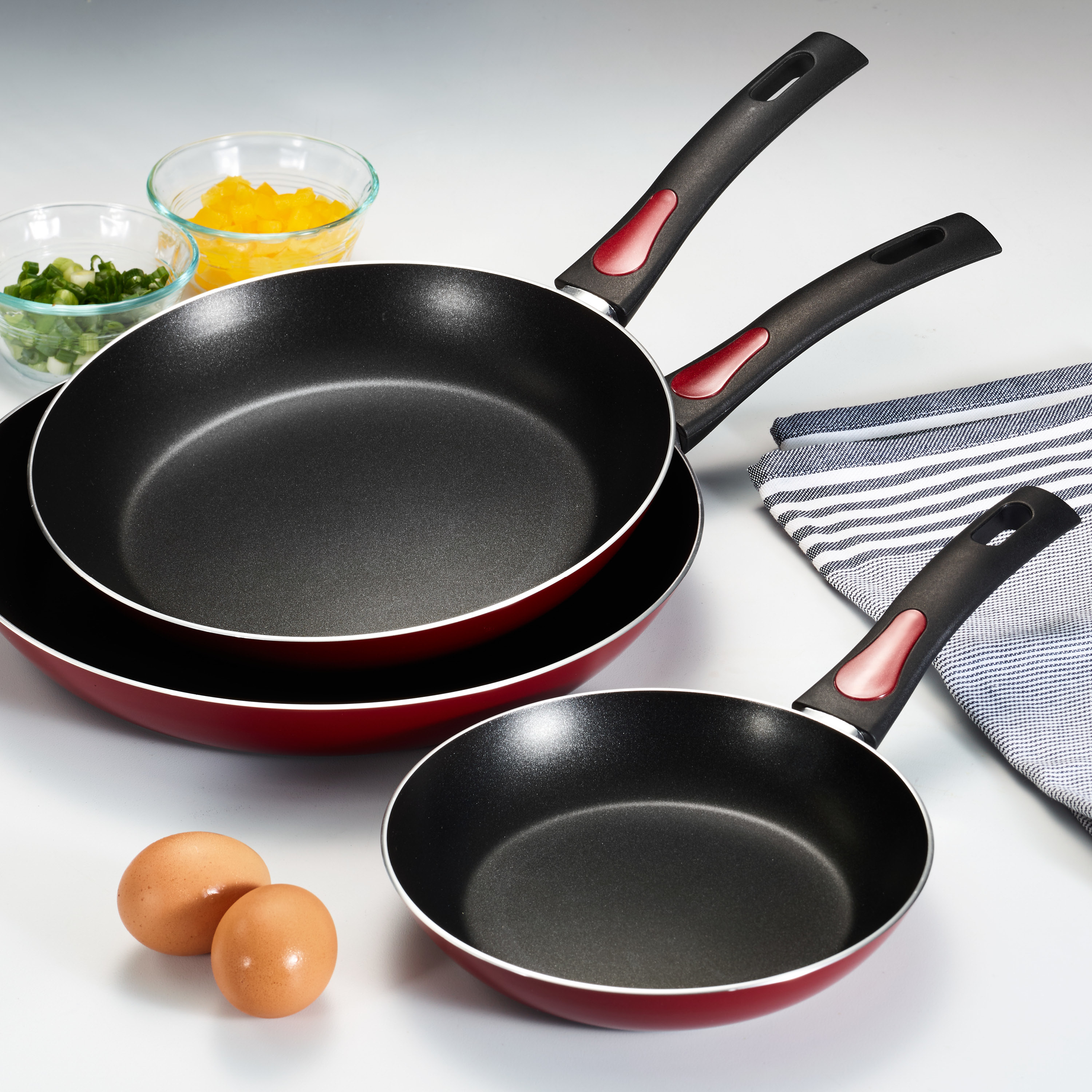 Three red and black fry pans in varying sizes