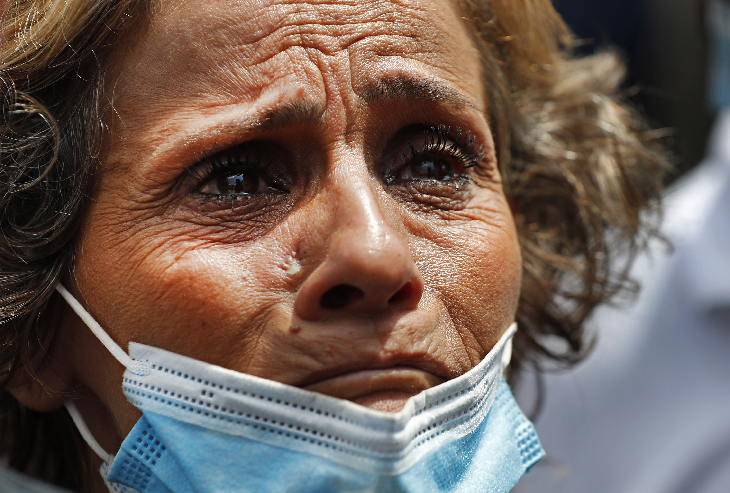 A crying woman wears a disposable blue mask pulled down to her chin