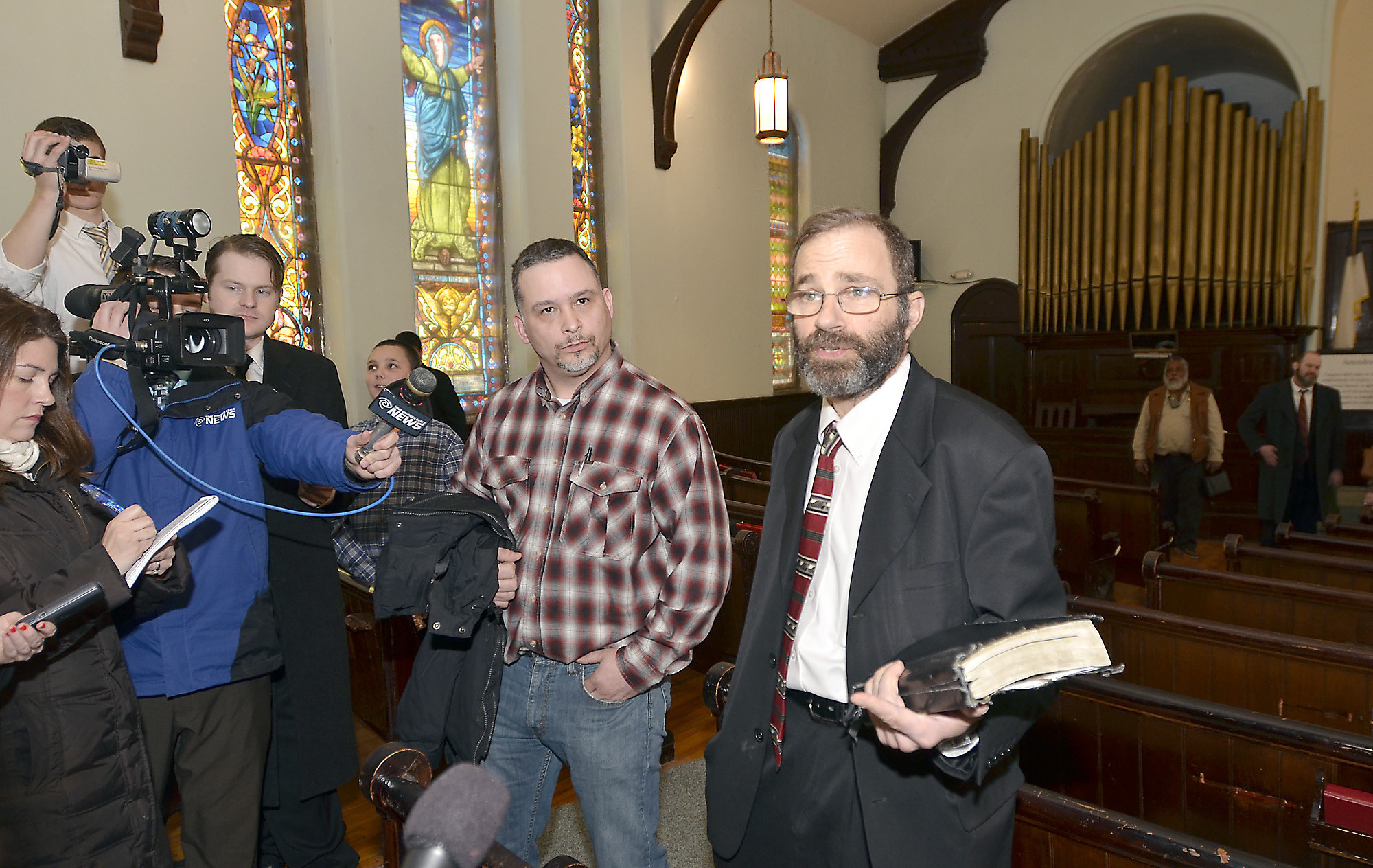 A camera crew interviews two men in a church. One holds a bible