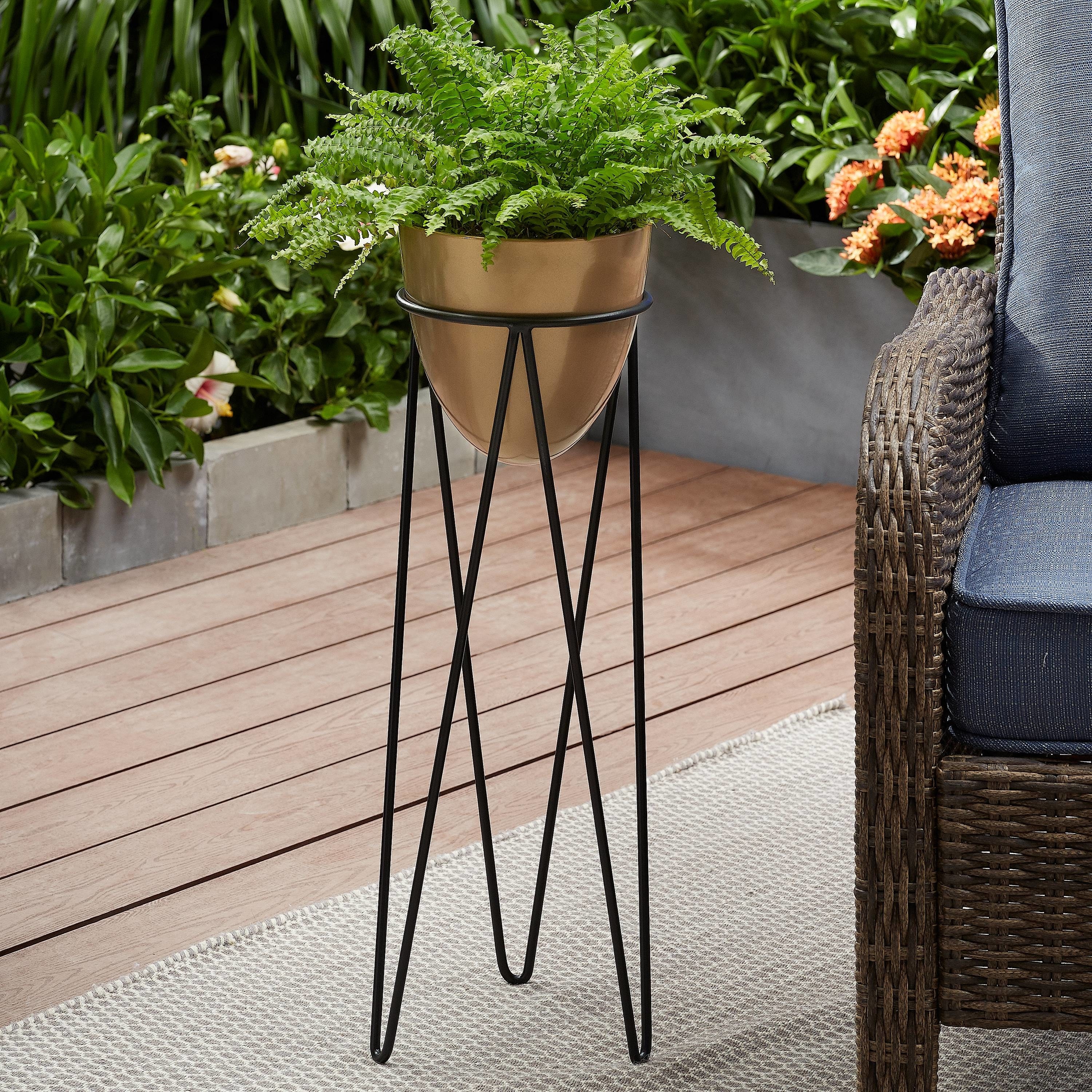 A brass-colored, bullet-shaped planter nestled in a black boho-style plant stand with hairpin legs