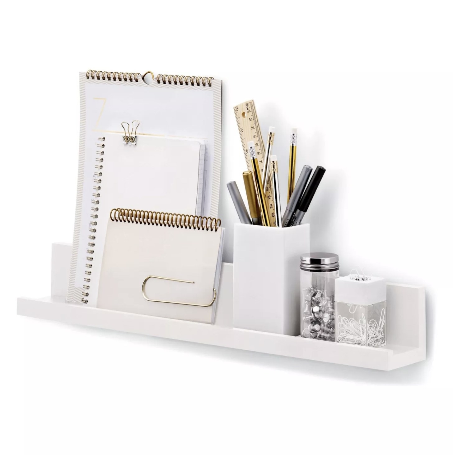 A white picture ledge holding notebooks, a cup of pens and pencils, a jar of pins, and a container of paper clips