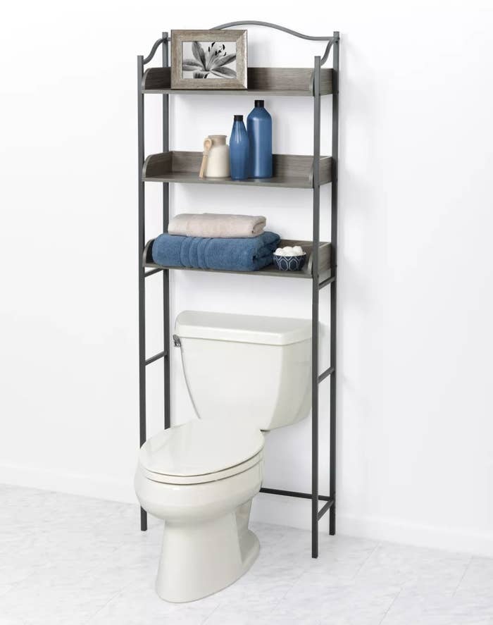 A shelving unit over the toilet with towels, vases, and a picture frame on the shelves