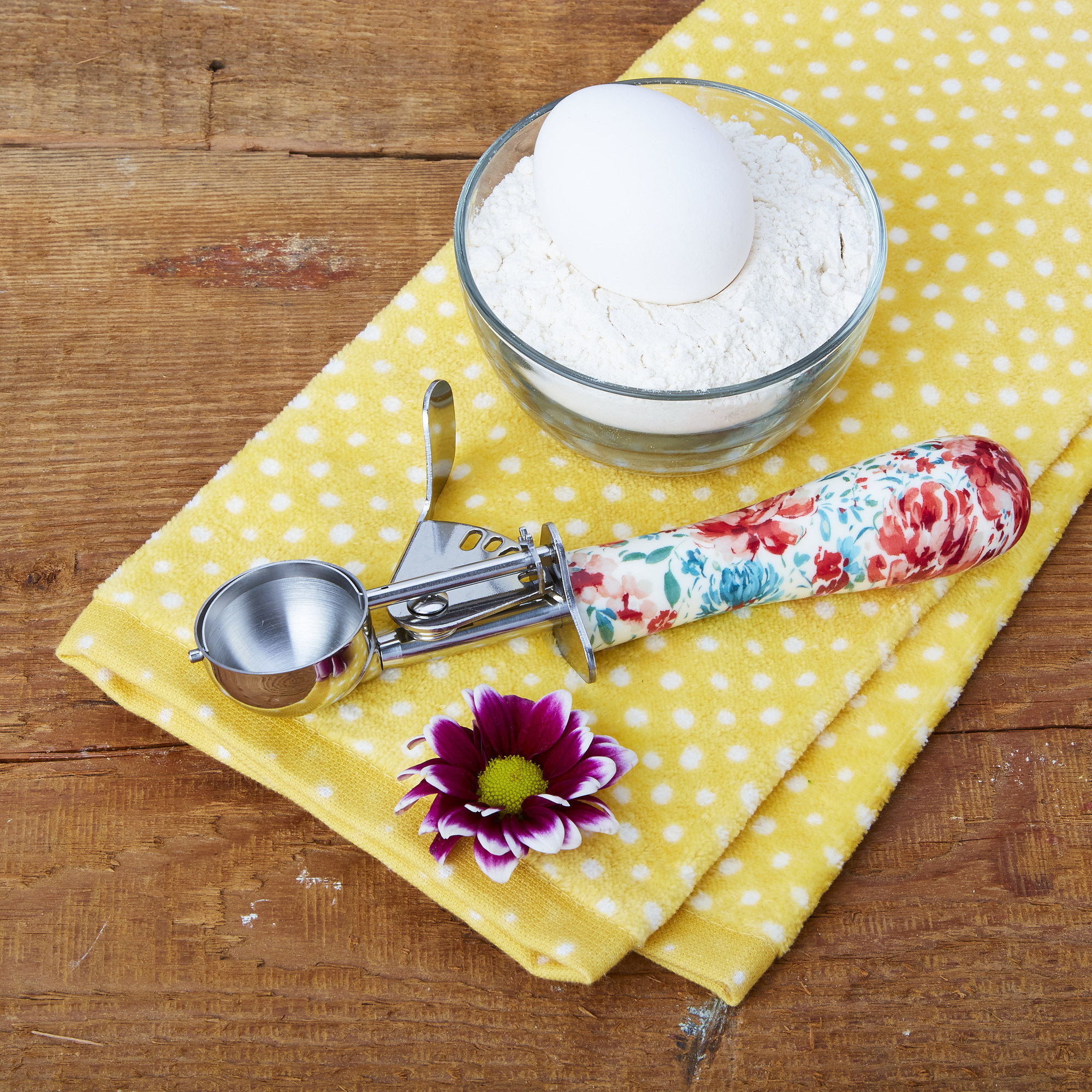 A silver and floral cookie scoop laying on a yellow hand towel