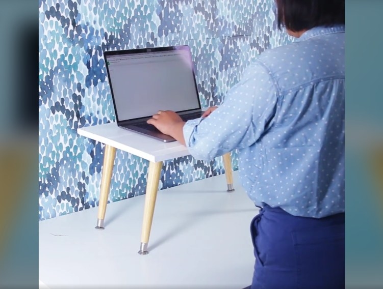 A person stands in front of the DIY raised desk attachment, typing on a laptop 