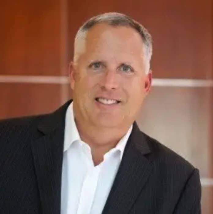 Mike Edwards wearing a suit and collared shirt smiles for the camera in a professional headshot.