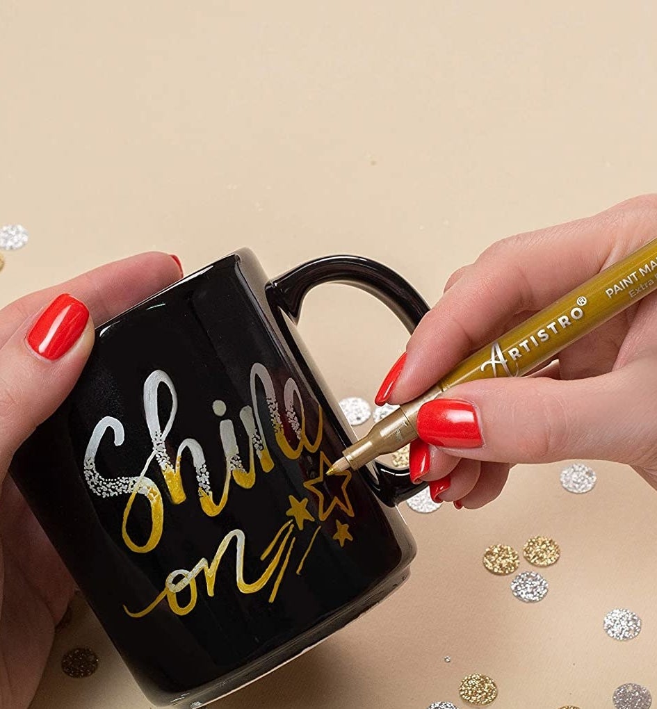A person writing on a mug with a metallic paint pen