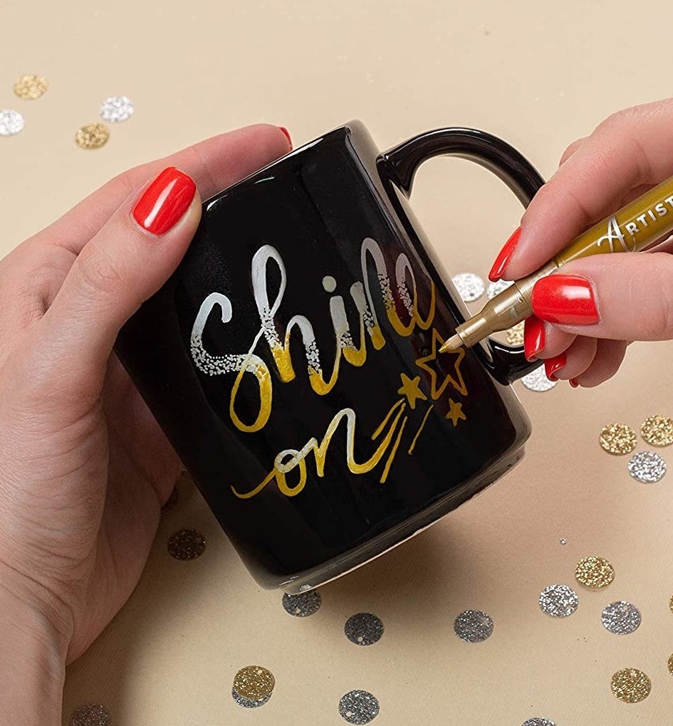A person writing on a mug with a metallic paint pen