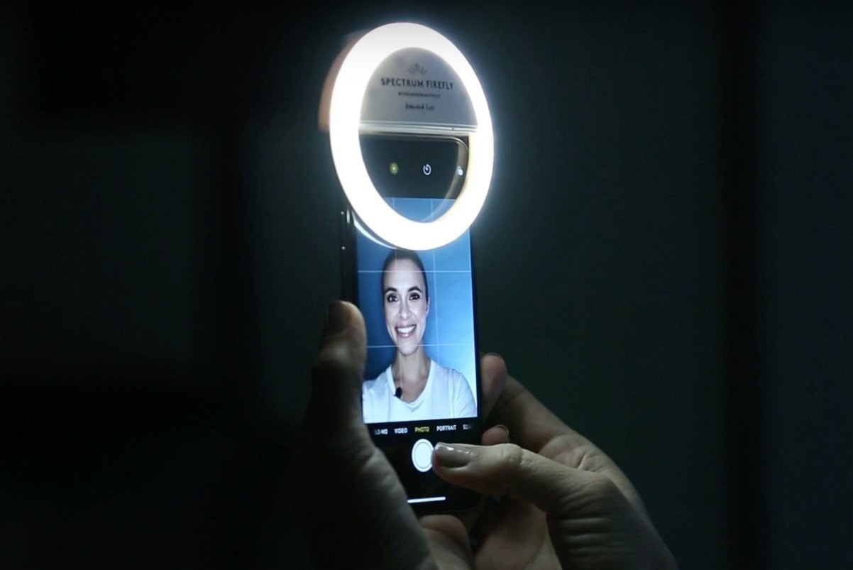 A woman smiles into the camera, a selfie light illuminating her face
