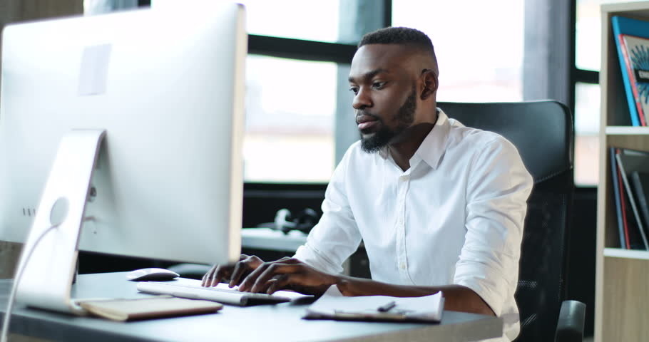 A Black man types on his desktop computer