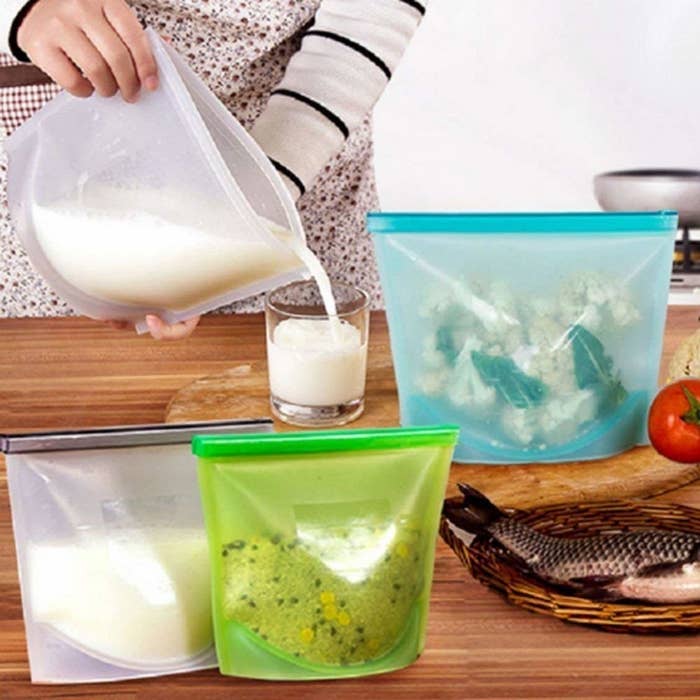 A person's hand pouring milk from the silicone bag into a glass, with other silicone bags around.