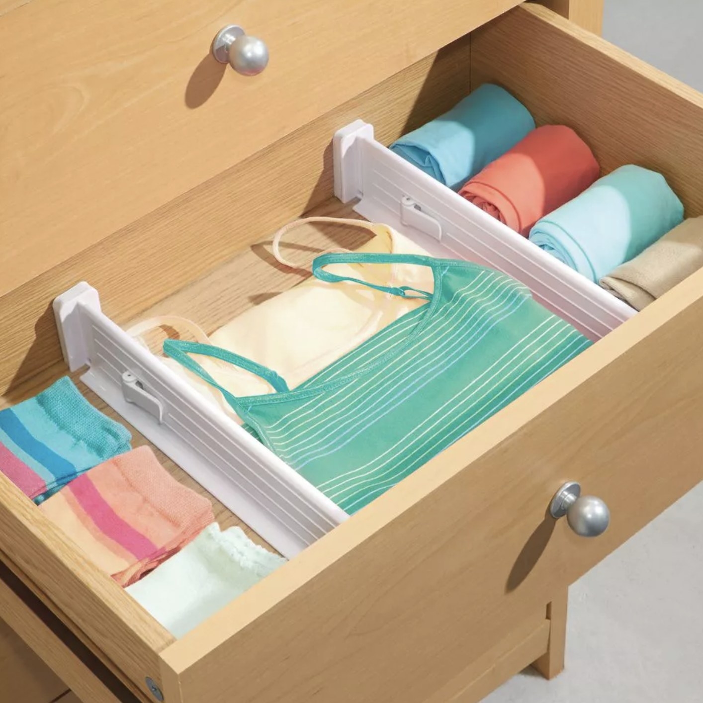 A drawer with two white dividers that have created a section for socks, a section for tank tops, and a section for rolled leggings.