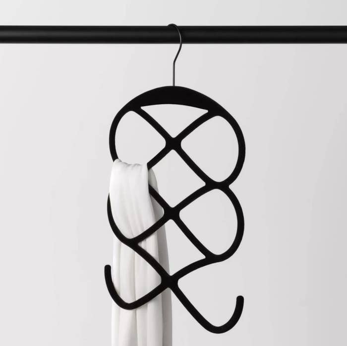 A black velvet hanger with six to eight slots holding one white scarf.