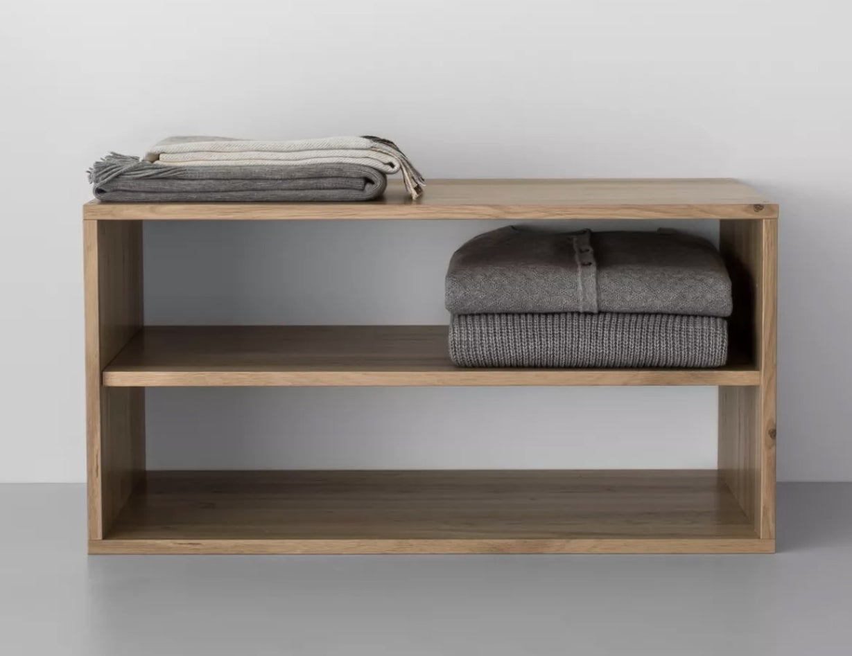 A wooden unit with three shelves holding two scarves and two sweaters.