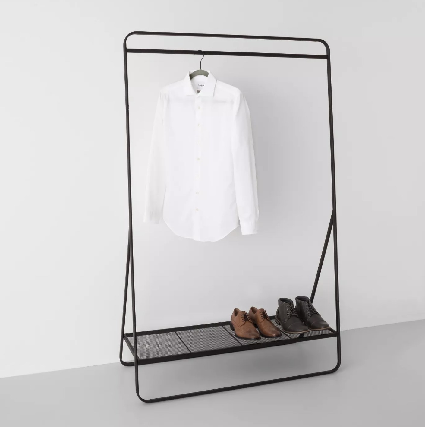 A black metal garment rack with a shelf holding two pairs of shoes and a rod holding a white button-down. 