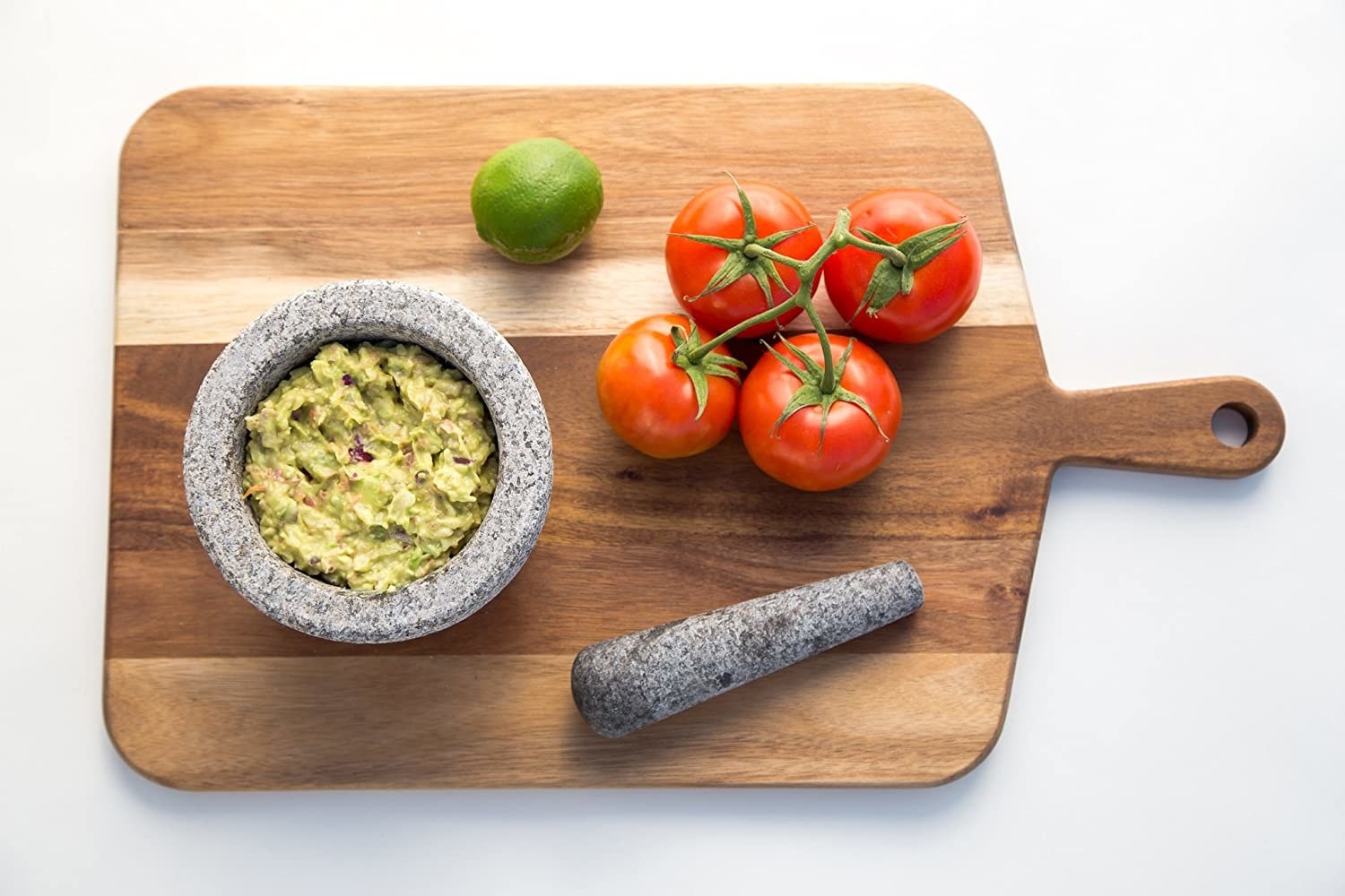 A wooden board with tomatoes a lime and guacamole in the mortar