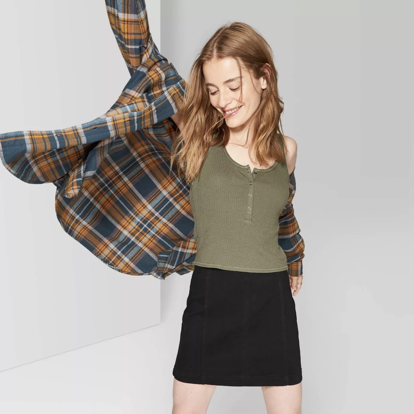 Model styles black skirt with green tank and plaid button down. 