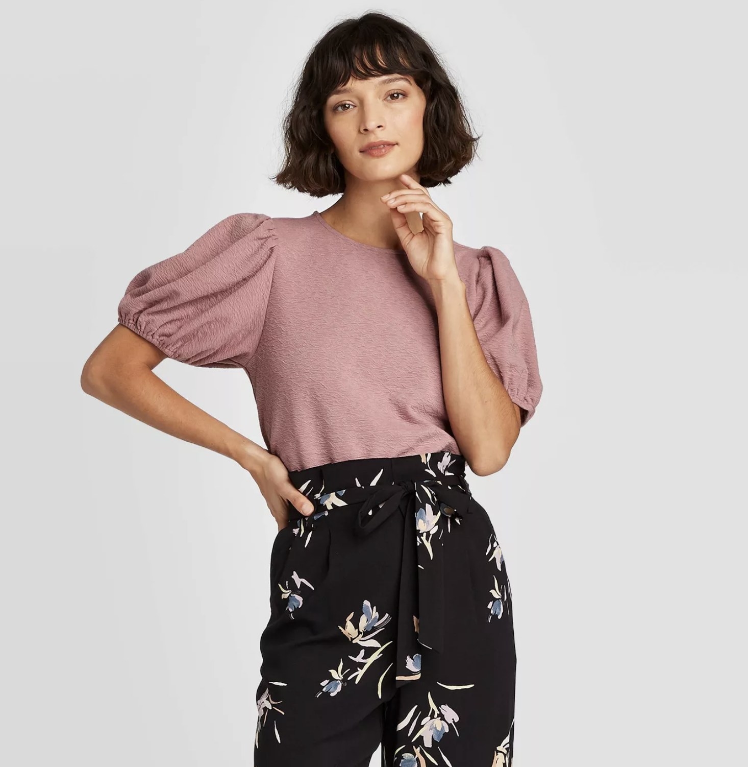Model poses in rose colored tee and patterned flowy pants. 
