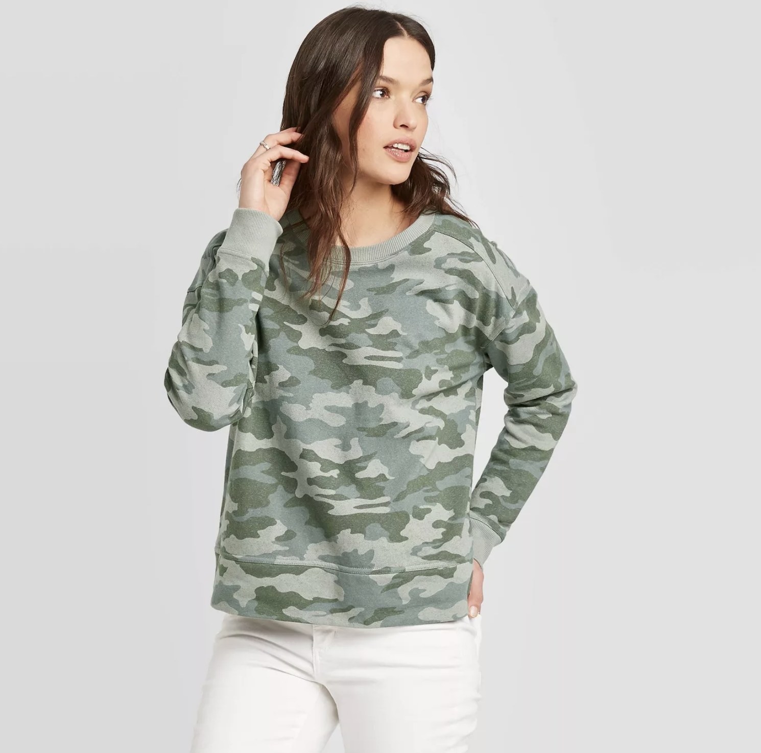 Model wears camo print crewneck with white jeans. 