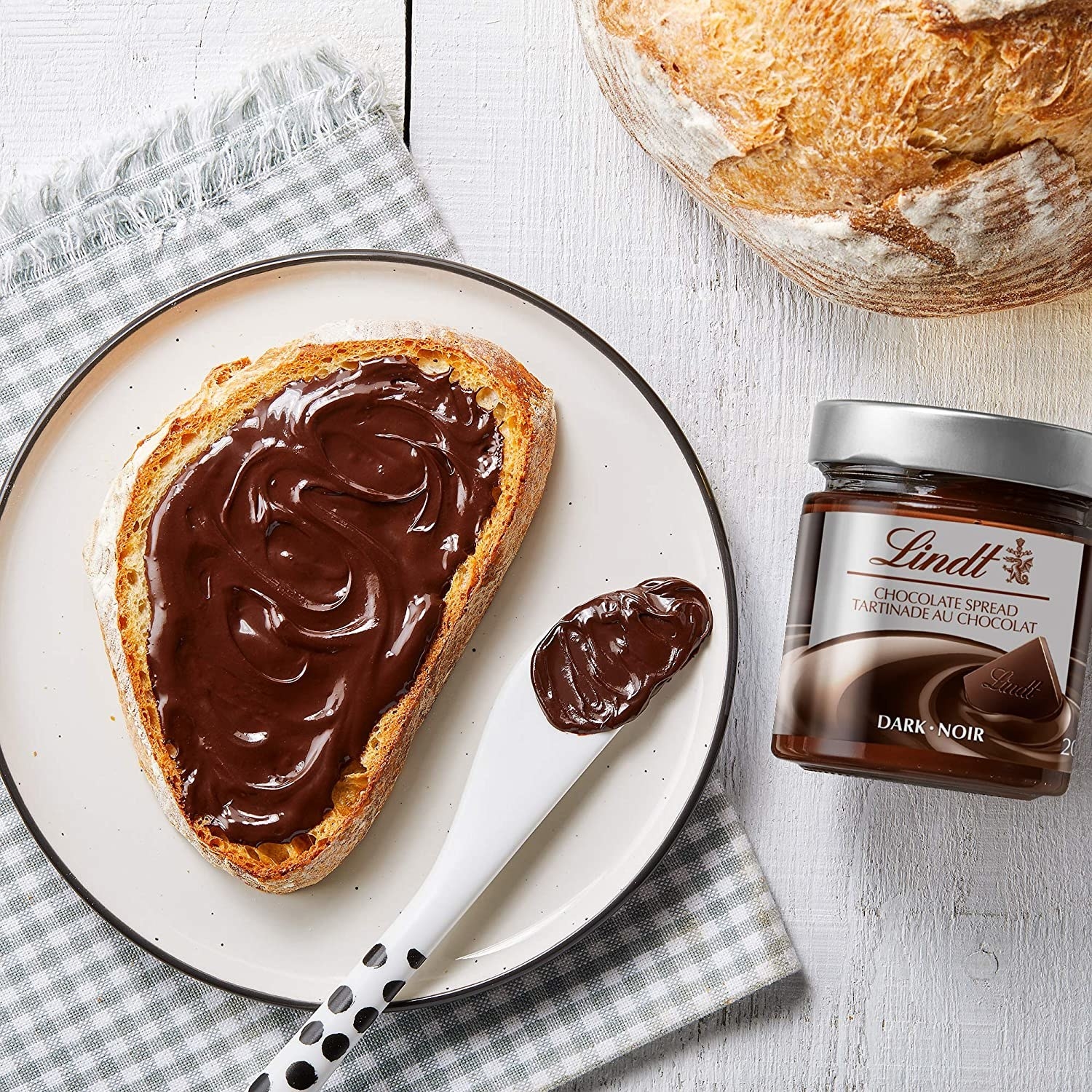 A piece of toast covered in Lindt chocolate spread next to the jar