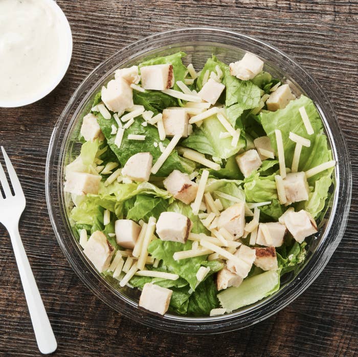 A Caesar salad with lettuce, cheese, and chicken bits