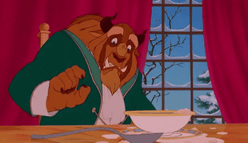 the Beast picks up a spoon and tries to use it in porridge as Belle looks on, surprised