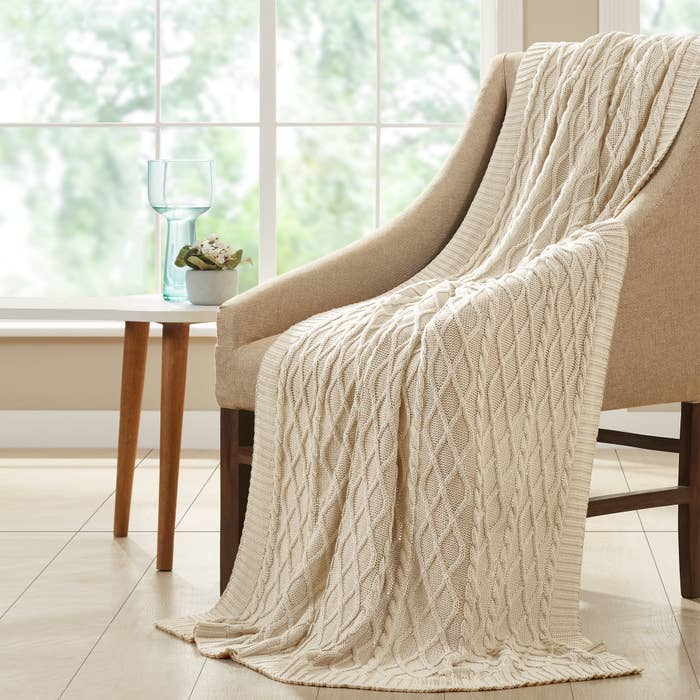 A beige cable knit blanket draped over a chair