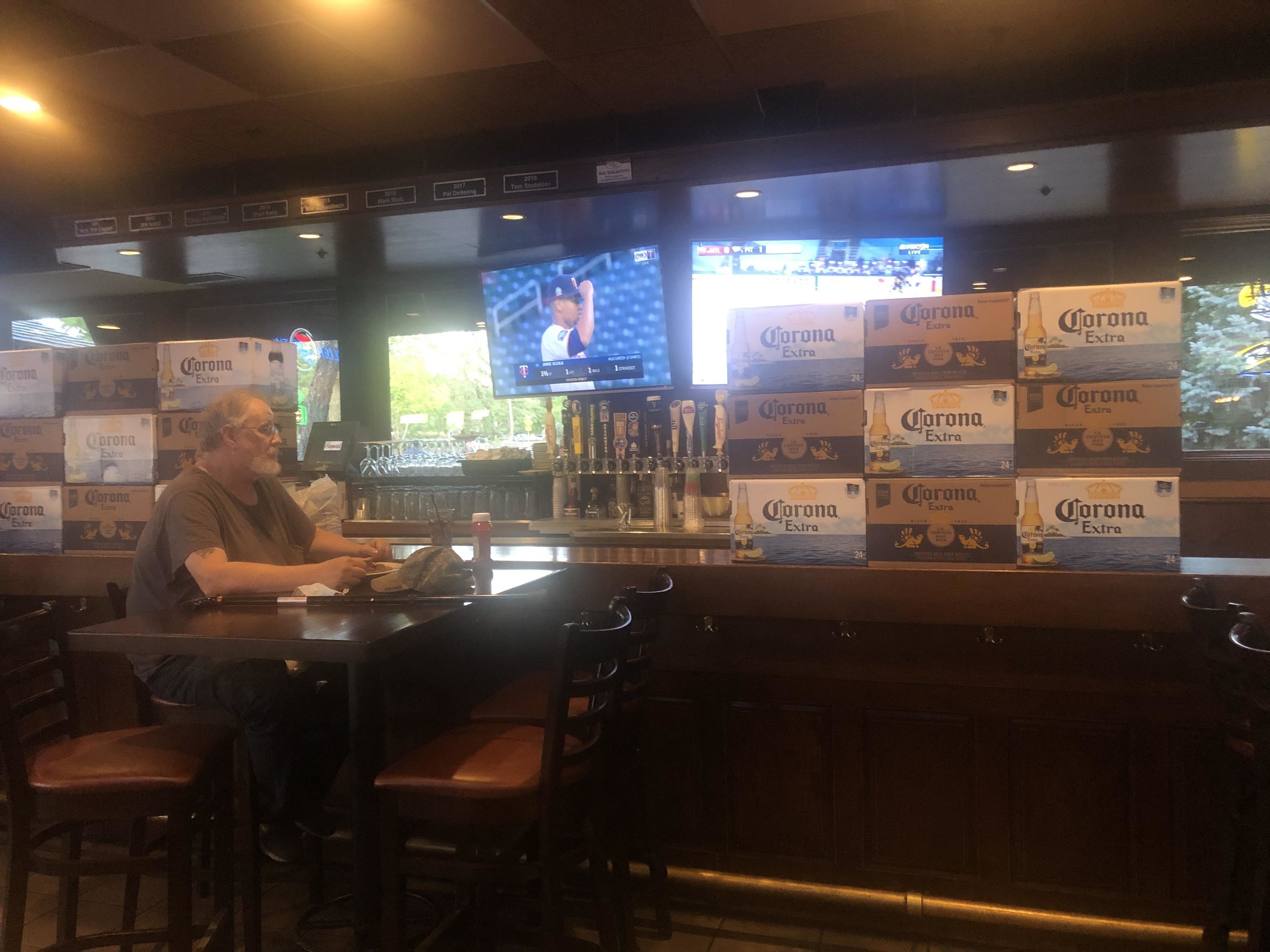 a patron at a bar, there are stacks of boxes of Corona beer on either side of him