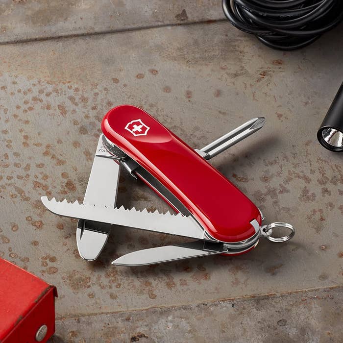 A red Swiss Army knife with a saw, screwdriver, and other tools partially opened