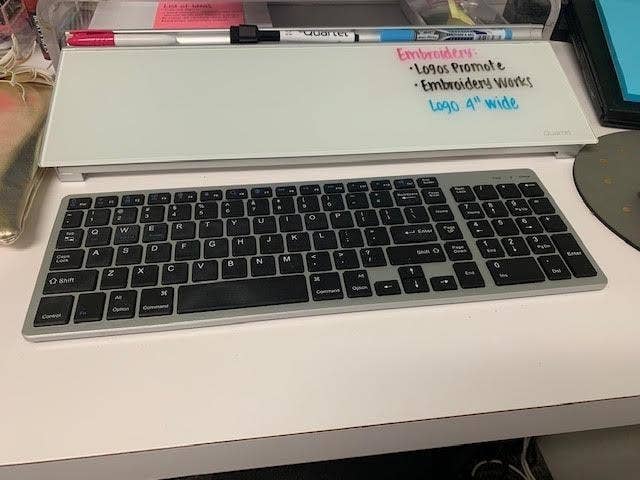 Reviewer's long rectangle-shaped whiteboard with groove across the top with markers in it in with a keyboard in front of it