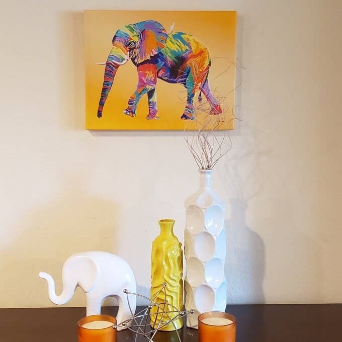 a canvas painting with a yellow background and elephant painted in all the colors of the rainbow