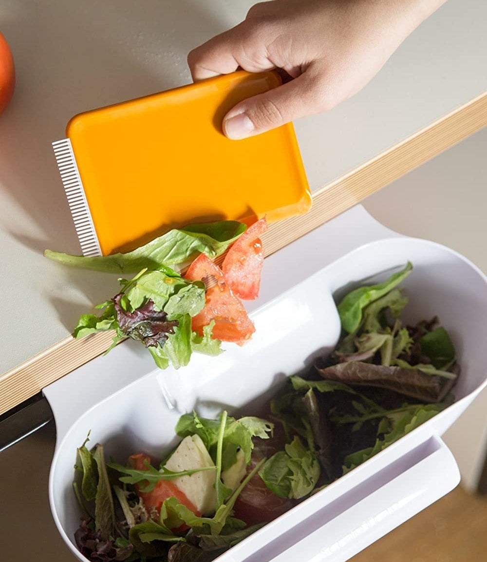 A person scraping salad into the scrap bin