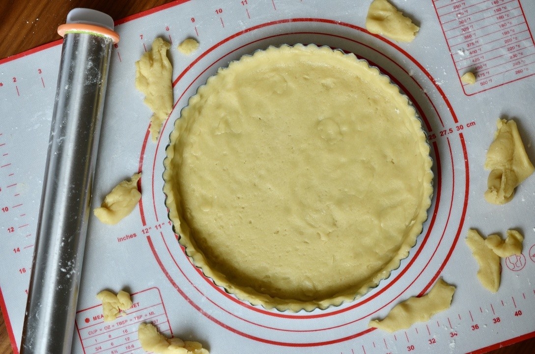 Dough molded to a tart pan next to a steel roller on a baking mat 