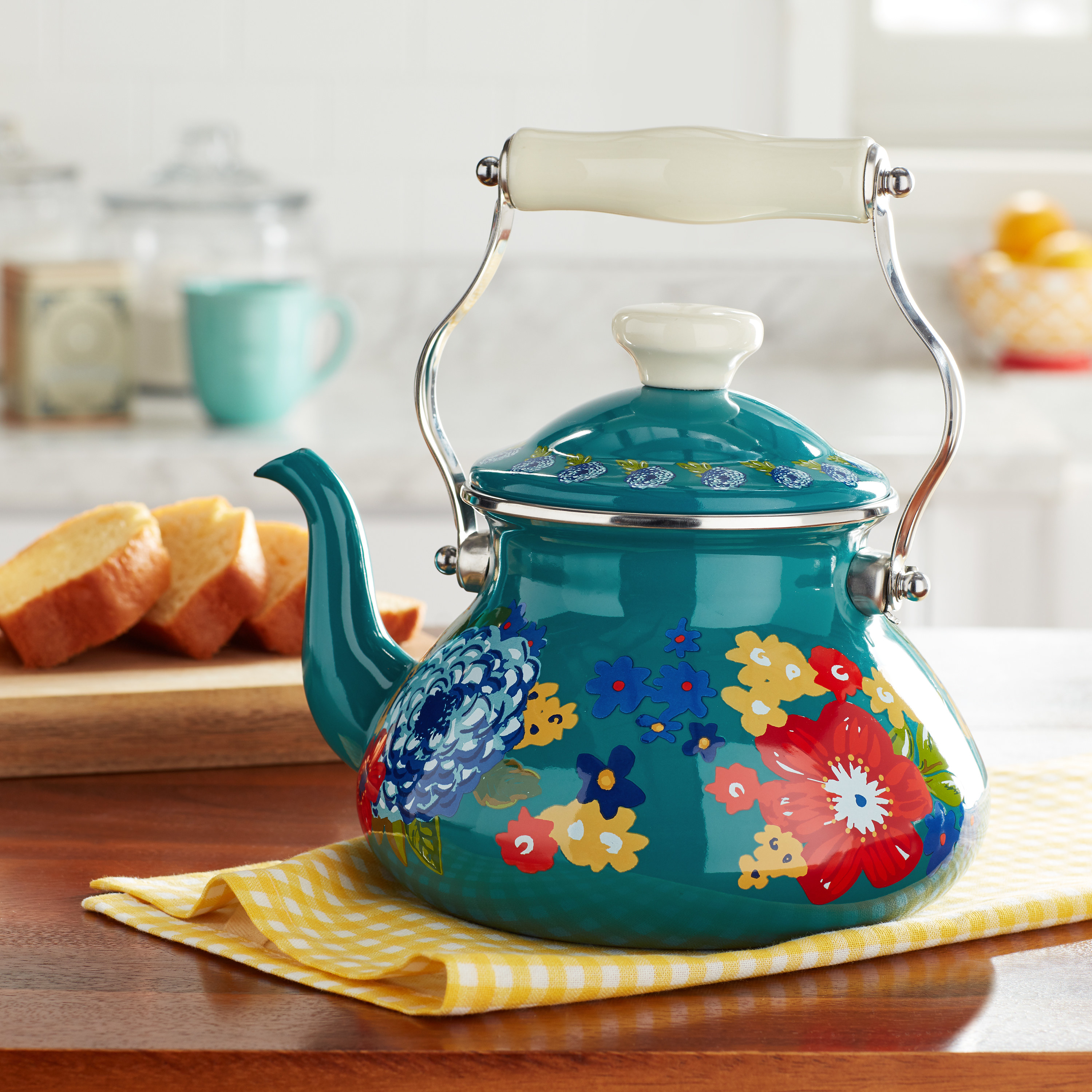 A teal tea kettle adorned with flowers sitting on a counter