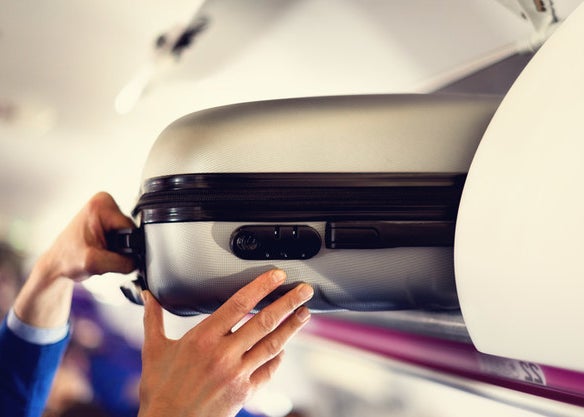 Hands pull a suitcase from an overhead carryon bin
