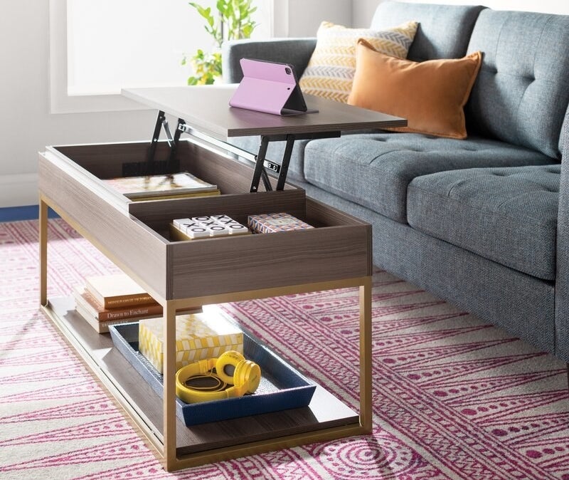 A gray wood coffee table with a lift-top and brass legs 