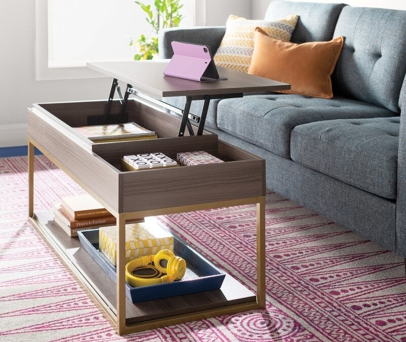 A gray wood coffee table with a lift-top and brass legs