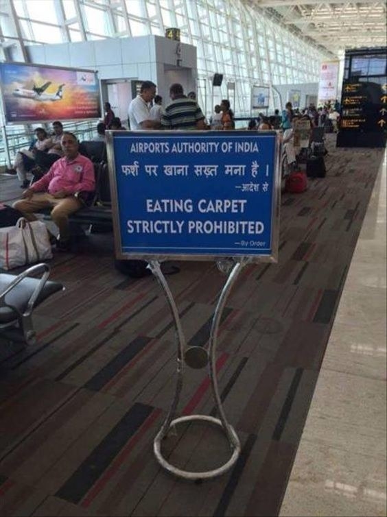 A busy airport in india and a sign in the terminal reads eating carpet strictly prohibited